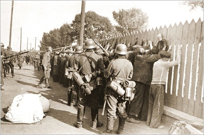 German soldiers round-up a group of Jewish men and line them up against a picket fence in Czestochowa